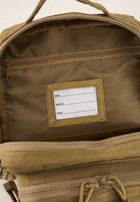 Rudas kuprinės vidus su užtrauktuku ir vardo etiketės skyriumi. Pagaminta iš tvirto audinio, su lygiu paviršiumi ir dviem raištelių uždarymo sistemomis.