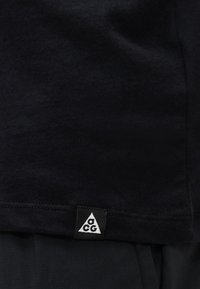 Μαύρο ύφασμα με μια μικρή μαύρη ετικέτα που φέρει ένα λευκό τρίγωνο και τα γράμματα "a," "c," και "g" σε μαύρο μέσα στο τρίγωνο.