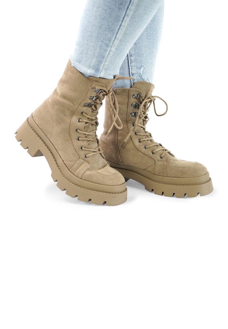 Tan suede ankle boots with a chunky tread sole, lace-up front, and metal eyelets. Textured and durable with a robust design.