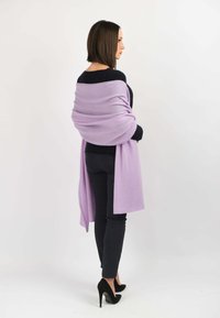 Lavendel sjal draperet over skuldrene, lavet af blødt stof med en glat tekstur. Båret med en sort sweater og bukser, suppleret med hæle.
