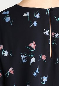 Tessuto nero con un motivo floreale che presenta fiori blu, rosa e bianchi. Include una piccola apertura sul retro chiusa con un bottone.