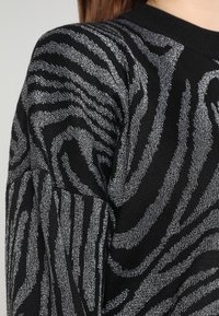 Schwarzer Pullover mit Zebrastreifenmuster in silberner Faden. Strukturierte Strickware mit rundem Halsausschnitt und langen Ärmeln.