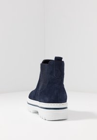 Námořnické sametové kotníkové boty s elastickými bočními panely, bílou podrážkou a modrým pruhovaným detailem. Obsahují poutko vzadu pro snadné obouvání.