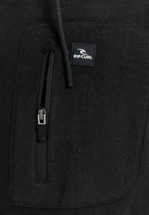 Zwarte fleece jack met een ritszak op de borst, een gestructureerde stof en een klein zwart-wit logopatch.