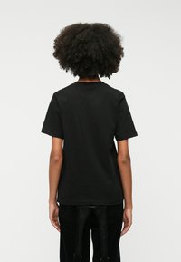 Μαύρη βαμβακερή μπλούζα με κο�ντά μανίκια, στρογγυλή λαιμόκοψη και χαλαρή εφαρμογή. Απλός σχεδιασμός, χωρίς ορατά μοτίβα ή λεπτομέρειες.