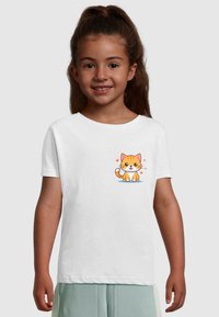 Hvid kortærmet t-shirt med en tegneserieagtig orange kat med et smilende udtryk og omgivet af hjerter, sat mod en ensfarvet baggrund.