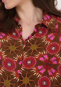 Bruine knop-overhemd met levendige roze, rode en gele patronen, met cirkelvormige motieven en lederen accenten. Korte kraag.