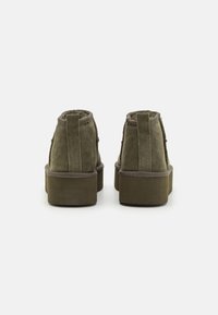 Green suede ankle boots with a rounded toe, textured surface, and a chunky platform sole. Features a pull tab at the back for easy wear.