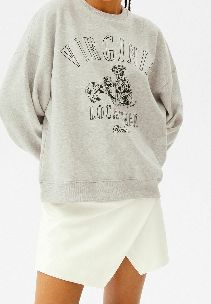 Šedá mikina s černou grafikou dvou psů a textem "VIRGINIA LOCATTEAM RICH." V kombinaci s bílou zavinovací sukní. Bavlněný materiál, volný střih.
