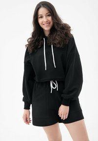 Czarna krótka bluza z kapturem, z regulowanym sznurkiem i dwiema kieszeniami z przodu, w połączeniu z czarnymi szortami posiadającymi kieszenie boczne i luźny krój.