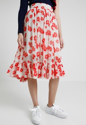 Weißer plissierter Midirock mit rotem Blumenmuster und Rüschensaum, kombiniert mit weißen Sneakers und einem marineblauen Oberteil.