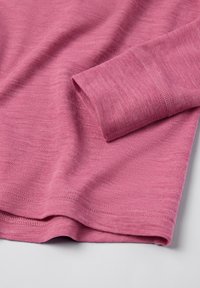 Lähellä vaaleaa taustaa oleva vaaleanpunainen pitkähihaisessa paidassa näkyy hihansuun ja helman pehmeä, tekstuuri neulekangas.