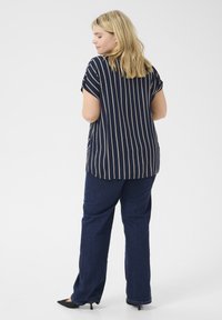 Blouse rayée marine à manches courtes, associée à un pantalon en denim bleu foncé. Parmi les détails notables figurent des rayures verticales et une coupe décontractée.
