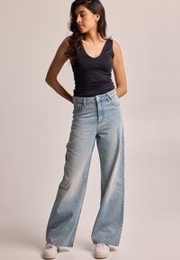 Top negro sin mangas, vaqueros de pierna ancha de cintura alta en azul claro, zapatillas blancas, tela suave, ajuste relajado, lavado desgastado, diseño minimalista.