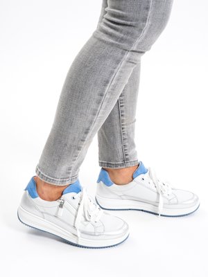 White sneakers with blue accents and laces worn with light grey fitted jeans, captured from side and back angles on a white background.