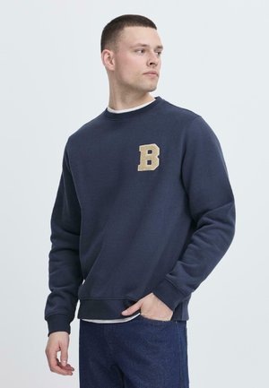 Navy sweatshirt van zachte stof, met een getextureerde gouden letter "B" op de linkerborst, ronde hals en geribbelde manchetten en onderkant.