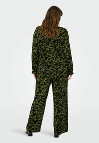 Zelený a černý vzorovaný dvoudílný outfit s dlouhými rukávy a širokými kalhotami. Texturovaná tkanina s abstraktními tvary po celém povrchu.