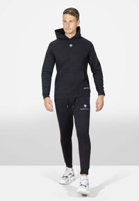 Felpa nera con cappuccio e tasca frontale, con logo sul petto, abbinata a pantaloni jogger coordinati con dettagli logo e polsini a coste.