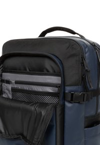 Marineblauwe rugzak met een gestructureerde zwarte bovenkant. Heeft meerdere met rits afgesloten vakken, gaaszakken en een stevige handgreep.