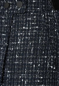 Marint strukturerad tyg med vita fläckar, som har ett vävt mönster. Två svarta cirkul ära knappar synliga nära toppen. Slät yta med strukturerad väv.