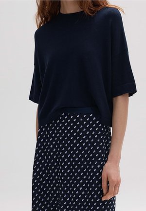 Granatowa dzianinowa bluzka o luźnym kroju, z krótkimi rękawami i okrągłym dekoltem, zestawiona z granatową spódnicą w kropki sięgającą kolan, w odcieniach granatu i lawendy.