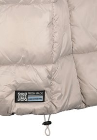 Jasno beżowa pikowana kurtka z przeszyciami, czarno-biała metka "Fresh Made" oraz regulowany sznurek z czarnym stoperem.