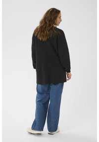 Oversized zwarte gebreide trui met lange mouwen, gecombineerd met loszittende blauwe denim jeans en lichte sneakers. Zachte textuur en relaxte pasvorm.