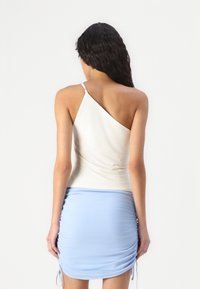 White asymmetrical tank top with thin strap, paired with a light blue ruched mini skirt featuring drawstring details. Smooth texture, casual design.