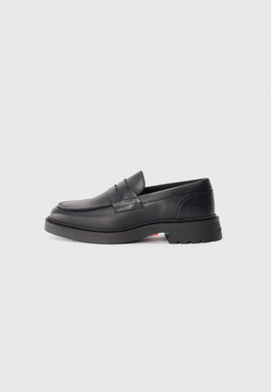 Black leather loafers with a rounded toe, a raised seam, and a thick rubber sole. Simple design with minimal branding on the side.
