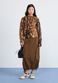 Brown and black patterned knit sweater, brown drawstring cargo skirt, black mini bag, and cream sneakers with black stripes.