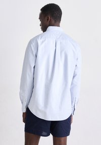 Lichtblauwe langemouwen overhemd van katoen, met een rugplooitje, knoopmanchetten en een klassieke kraag. Gestyled met donkere shorts.