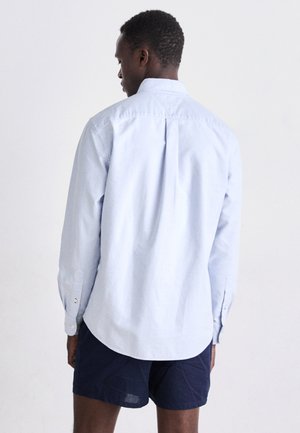 Camisa de manga larga azul claro hecha de algodón, con un pliegue en la parte posterior, puños con botones y un cuello clásico. Estilizada con pantalones cortos navy.