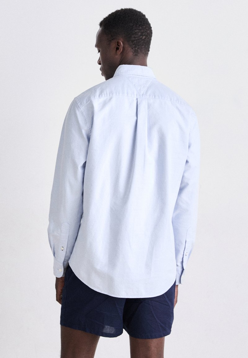 Lichtblauwe langemouwen overhemd van katoen, met een rugplooitje, knoopmanchetten en een klassieke kraag. Gestyled met donkere shorts.