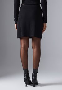 Jupe mini noire côtelée avec une taille ajustée, associée à des collants noirs transparents et des bottines. Design simple sans motifs visibles.