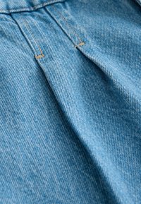 Svetlo modrá denim látka so štruktúrovaným tkaním, s viditeľným šitím a záhybmi. Materiál má jemný, opotrebovaný vzhľad.