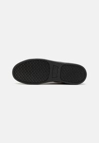 Fekete gumi sneaker talp, textúrált, szőtt mintázattal és kiemelkedő logó részlettel, ívelt formával és sima szélekkel.