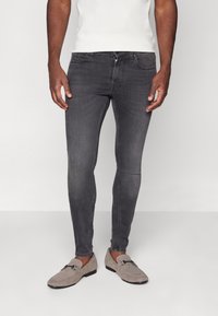 Grijze skinny jeans met een gladde textuur en subtiele vervaging, gecombineerd met grijze instapschoenen met een gespdetail.