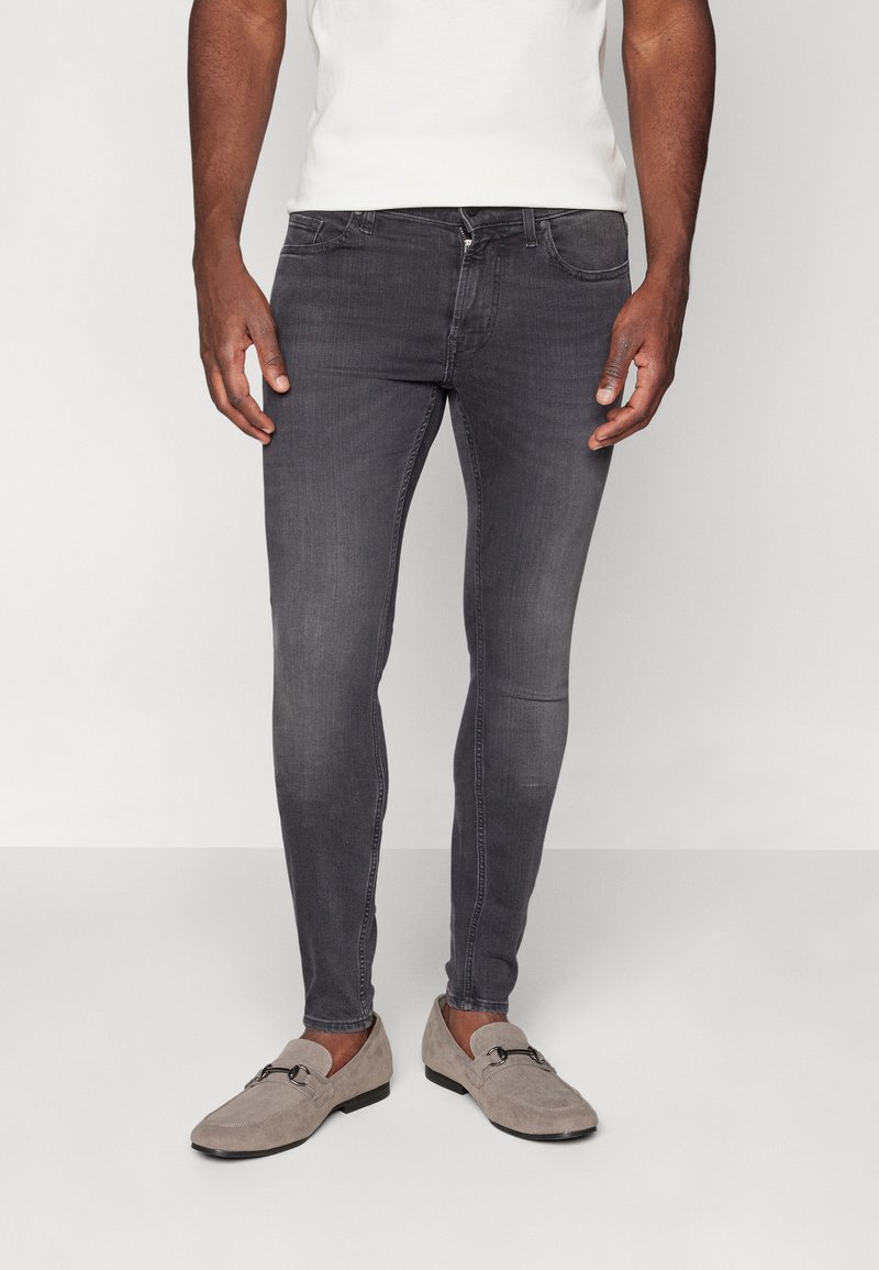 Grijze skinny jeans met een gladde textuur en subtiele vervaging, gecombineerd met grijze instapschoenen met een gespdetail.
