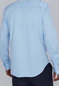 Jasnoniebieska koszula z długim rękawem, wykonana z gładkiej bawełnianej tkaniny, z zaokrąglonym dołem i mankietami zapinanymi na guziki, zapewniająca dopasowany krój.