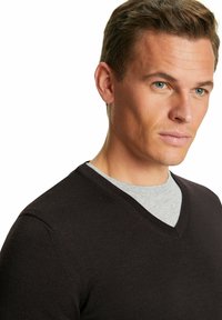 Maglione nero a scollo a V con texture a coste, indossato sopra una t-shirt grigia a collo rotondo. La vestibilità è slim e il tessuto appare liscio.