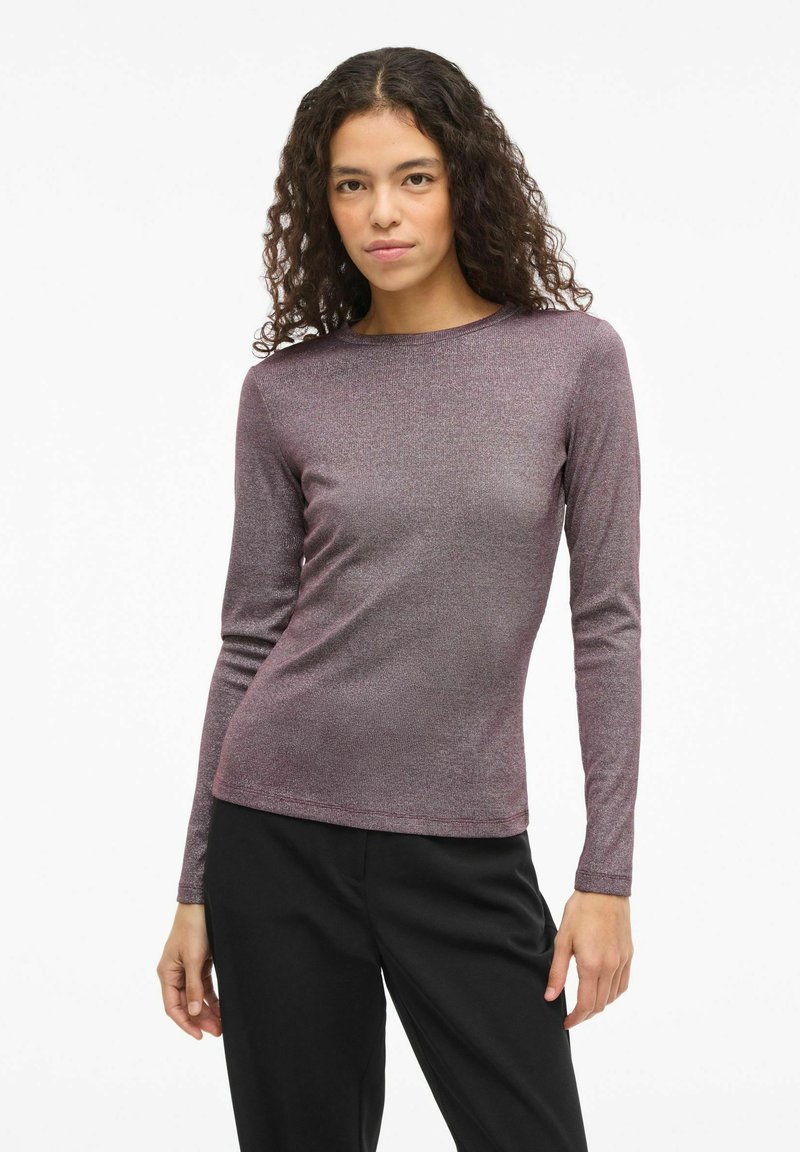 Top de manga larga y ajustado en tejido morado brillante con cuello redondo. Textura suave, se lleva con pantalones oscuros.