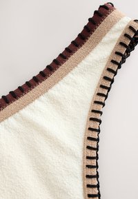 Gros plan d'un tissu blanc texturé avec une bordure beige et des détails de couture noire le long des bords et une couture intérieure bordeaux.