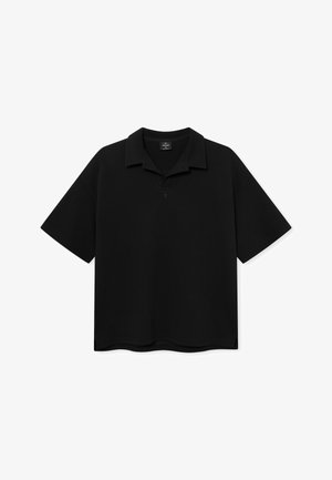 Polo shirt nera a maniche corte con colletto a pieghe, vestibilità ampia e logo discreto sul petto, presentata su uno sfondo bianco.