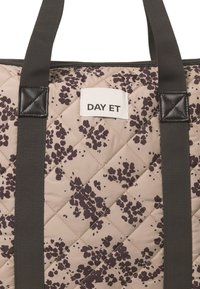 Quilted Tragetasche in Beige mit dunklem Blumenmuster, ausgestattet mit schwarzen Trägern und einem angenähten Etikett mit dem "DAY ET"-Logo. Strukturierte Oberfläche.
