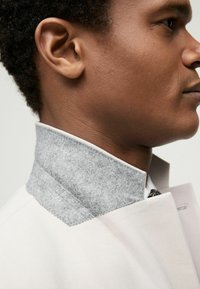 Chaqueta gris claro con un suave cuello de fieltro gris. El cuello tiene un acabado limpio, que contrasta con la textura suave de la tela de la chaqueta.