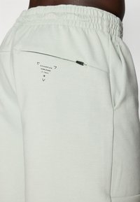 Pantalons de survêtement vert clair en tissu doux, avec une taille élastique et une poche zippée à l'arrière avec un détail de marque.