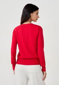 Suéter de punto rojo con cuello redondo, puños y dobladillo acanalados. La tela parece suave y ajustada, con mangas largas.