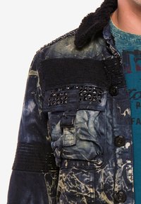 Jeansjacke mit schwarzem Kunstpelzkragen, ausgestattet mit gebleichten Mustern, strukturiertem Stoff, Tasche mit Schnallen-Detail und Nietenakzenten.
