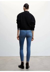 Suéter negro de punto con diseño texturizado, puños a rayas blancas y negras, combinado con jeans ajustados azules, que presentan una silueta entallada.