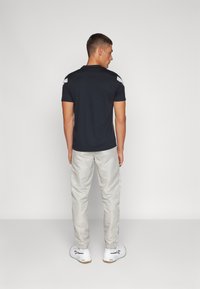 Camisa polo negra de hombre con mangas cortas, con detalles blancos en los hombros. Combinada con pantalones beige y zapatillas blancas.